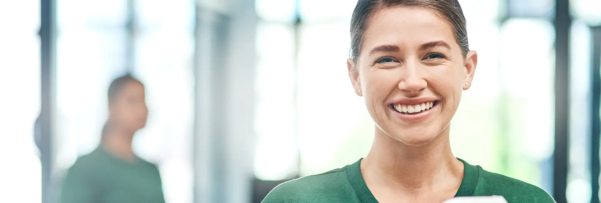 Büroreinigung - lächelnde junge Frau in grünem T-Shirt mit einem grauen Eimer vor sich mit Reinigungsutensilien in der Hand - Clean Team Reinigung von Büros