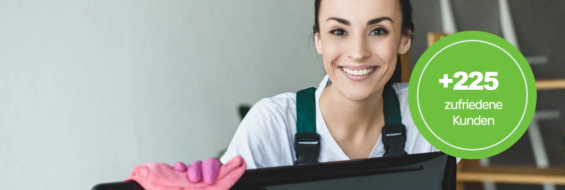 Reiningungsleistungen - Lächelnde Frau schaut in die Kamera und wischt einen Computer-Monitor mit einem rosafarbenden Lappen - Clean Team