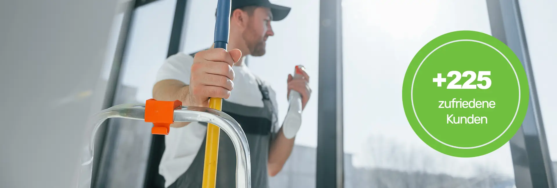 Gebäudereinigung - Mann mit Bart und blauer Mütze im grauen Overall putzt ein Fenster - Clean Team Solingen - Clean Team Wuppertal