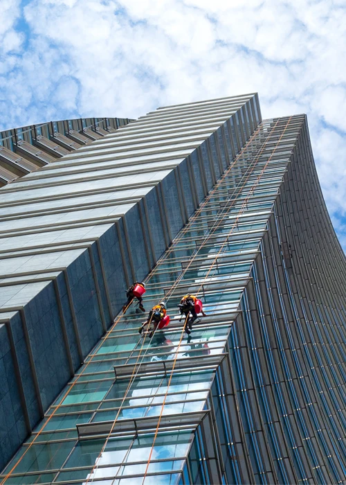 Unterhaltsreinigung - Hochhaus mit Glasfront wird von außen von drei Gebäudereinigern geputzt, die mit Seilen gesichert sind in großer Höhe - Clean Team Gebäudereinigung